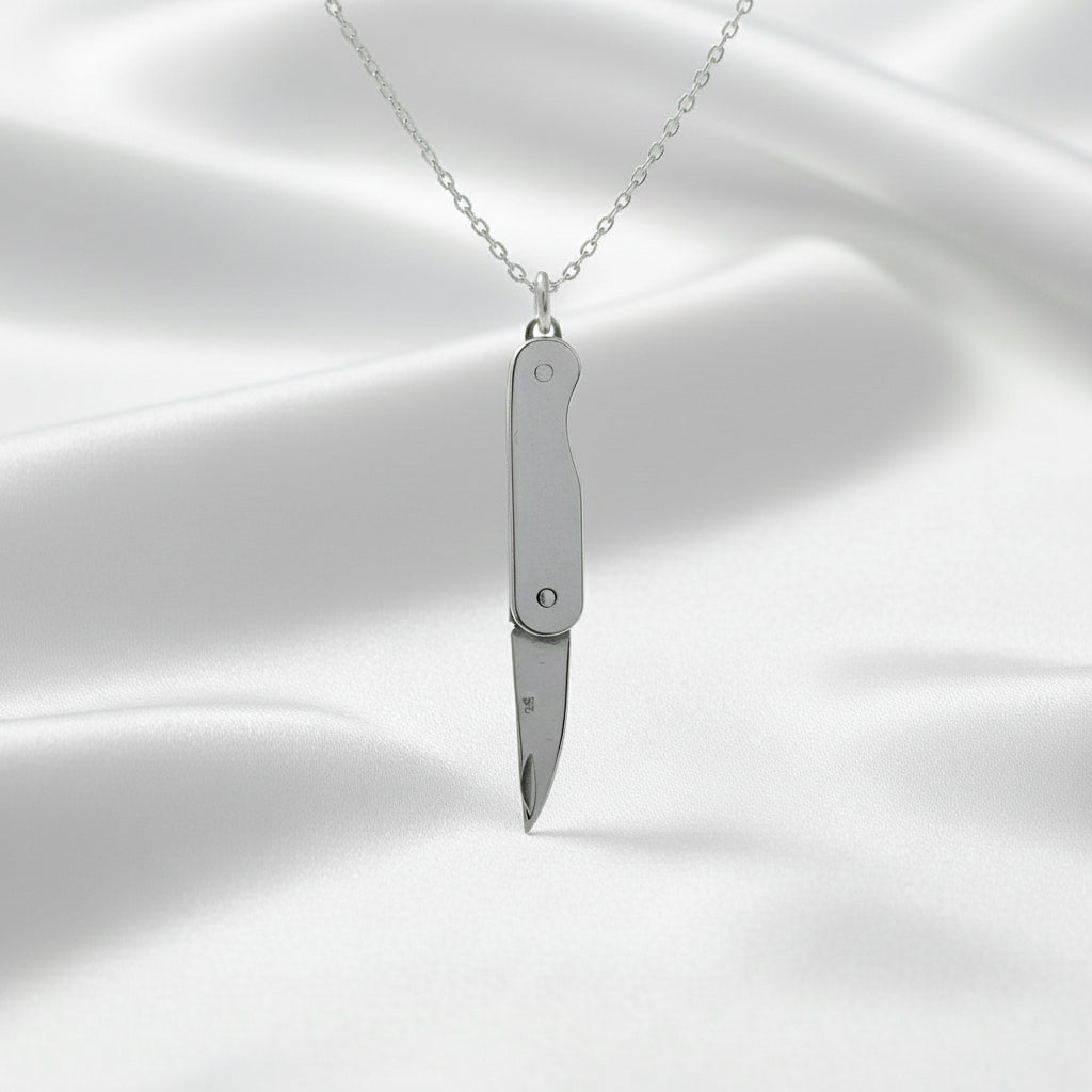 Silver knife-shaped pendant on a chain against a white satin background