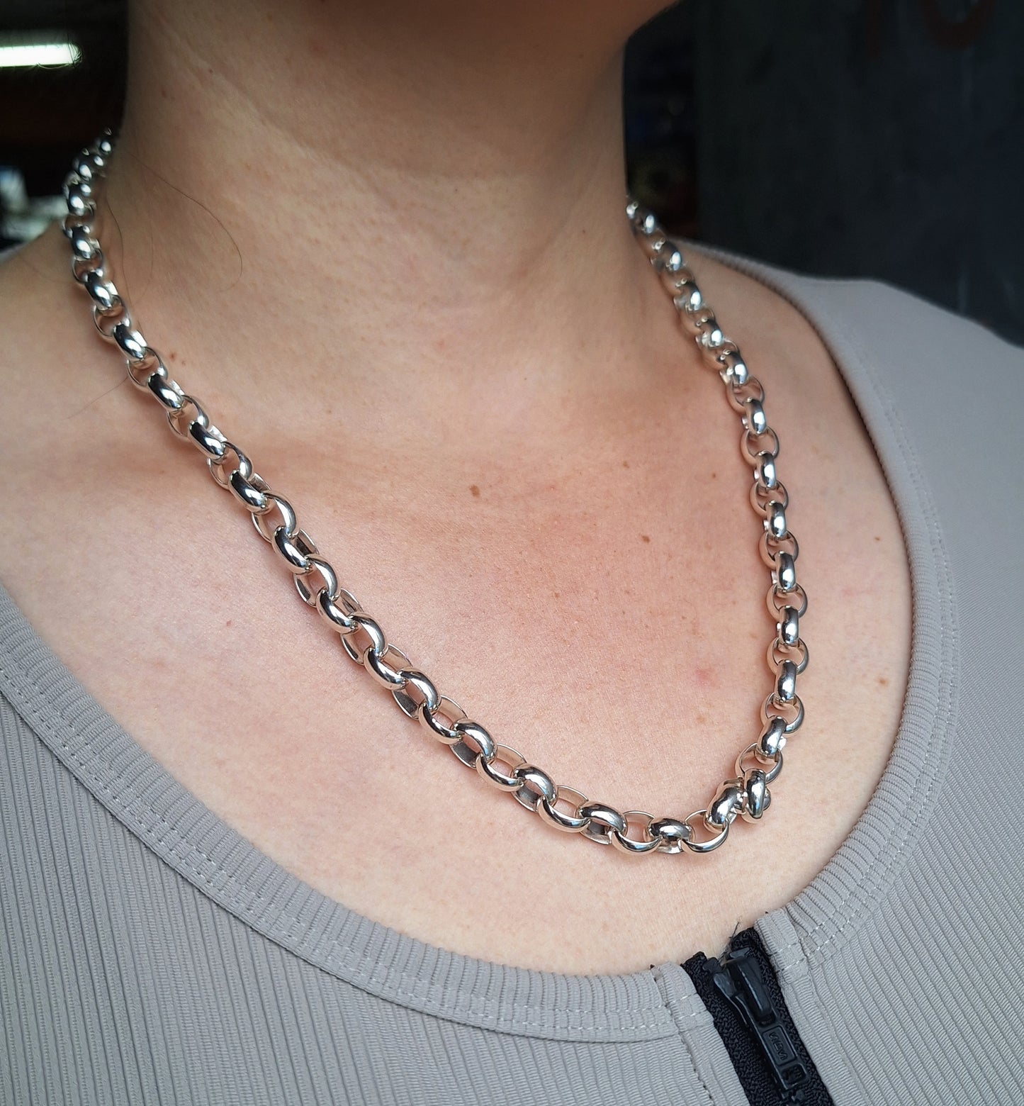 Silver chain necklace worn by a person with a blurred background