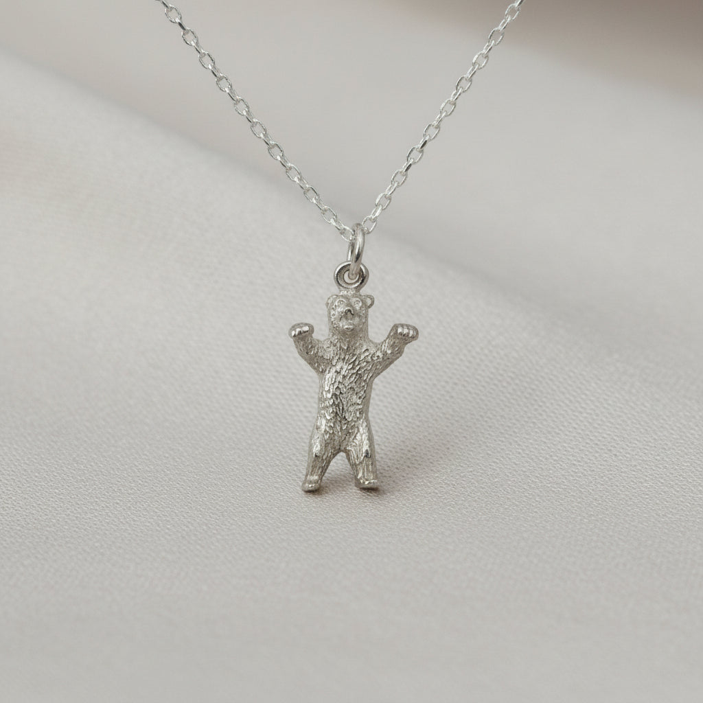 Silver bear pendant on a chain against a light gray background