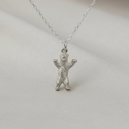 Silver bear pendant on a chain against a light gray background