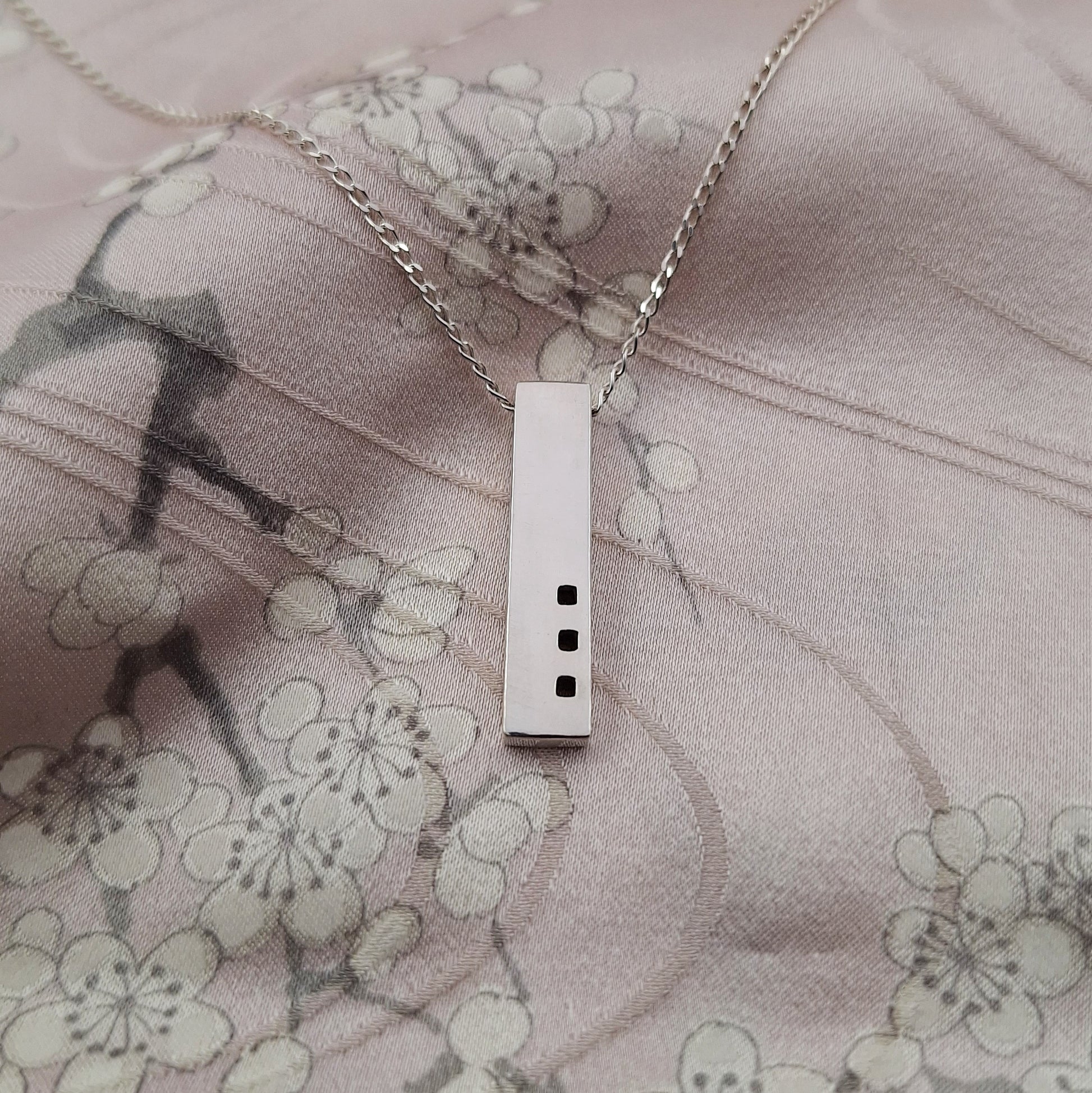 Silver necklace with a rectangular pendant on a floral fabric background