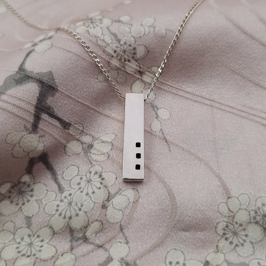 Silver necklace with a rectangular pendant on a floral fabric background