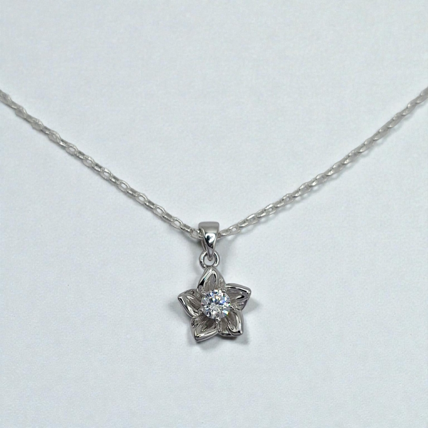 Silver necklace with a flower-shaped pendant on a light gray background
