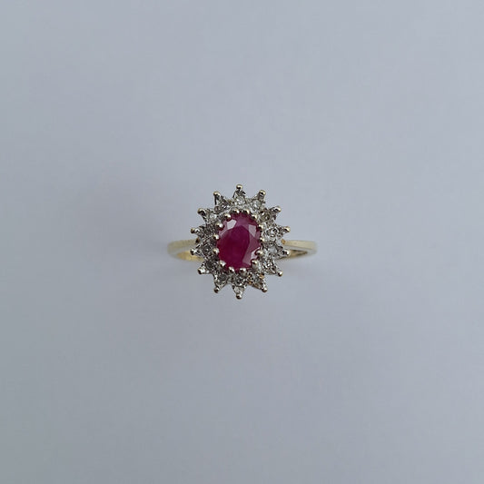 Gold ring with a red gemstone and diamond accents on a light gray background