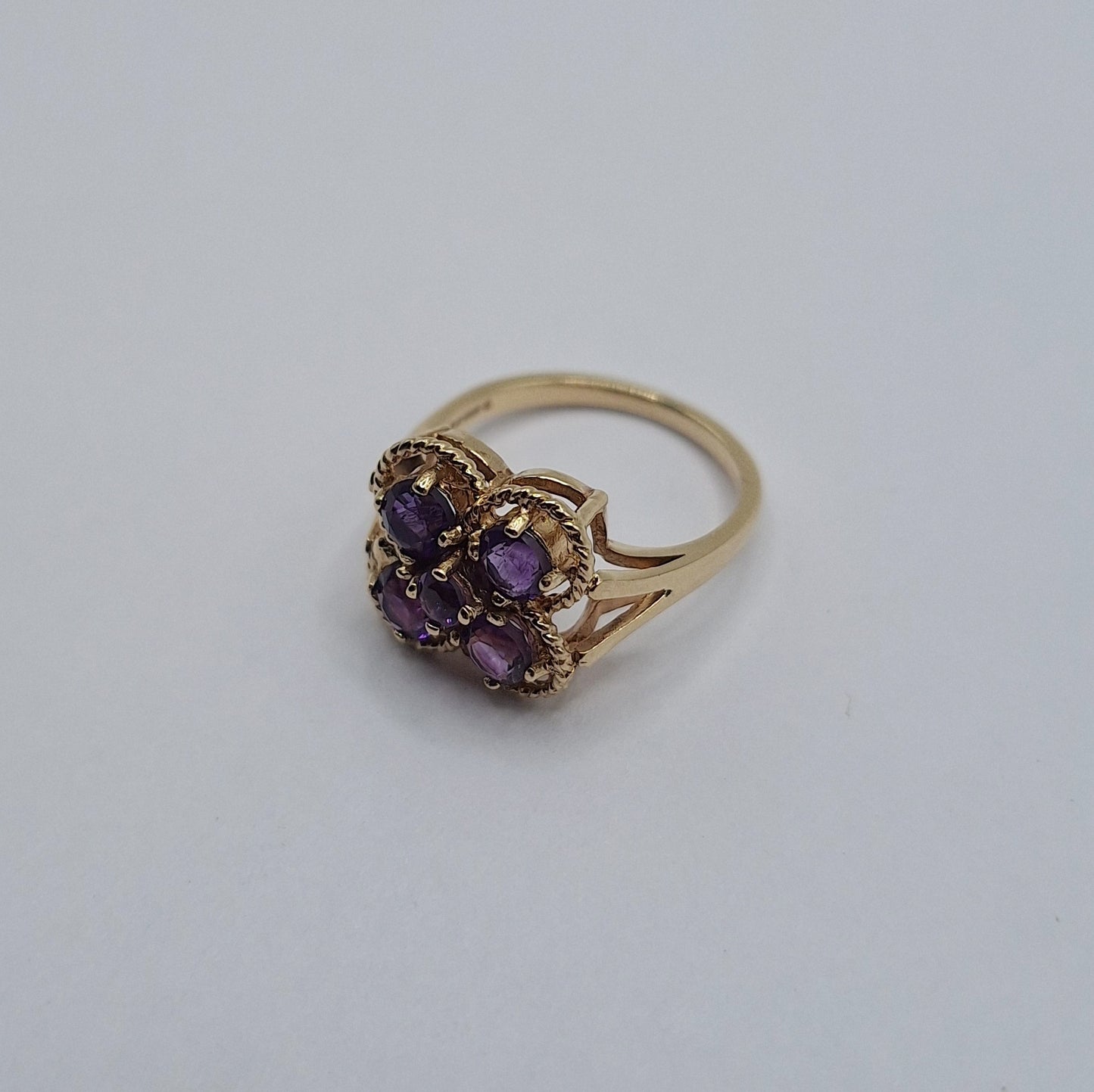 Gold ring with purple gemstones on a light gray background